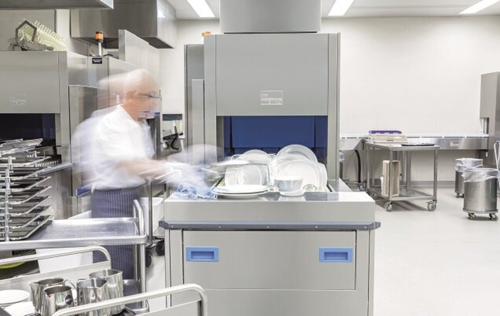 An employee uses a MEIKO industrial dishwasher in a back-of-house kitchen environment