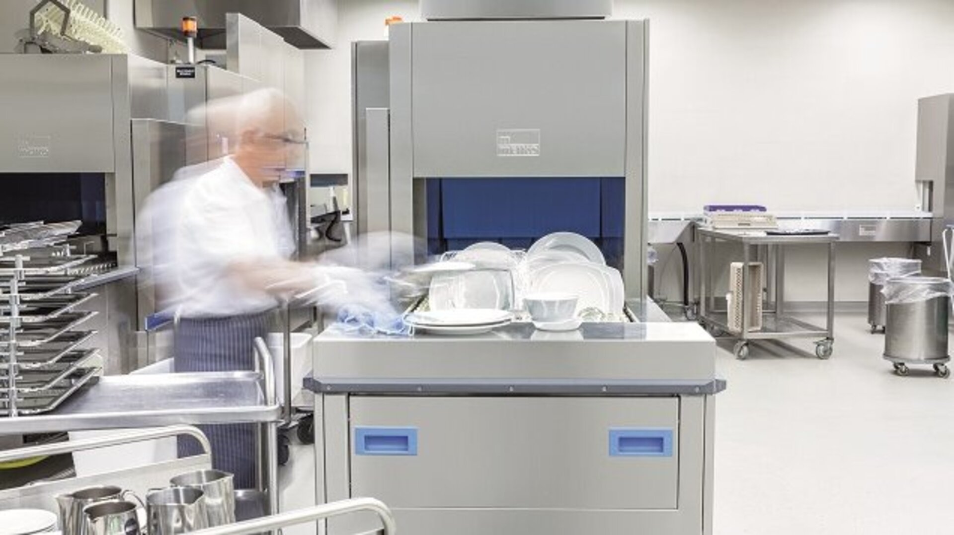 An employee uses a MEIKO industrial dishwasher in a back-of-house kitchen environment